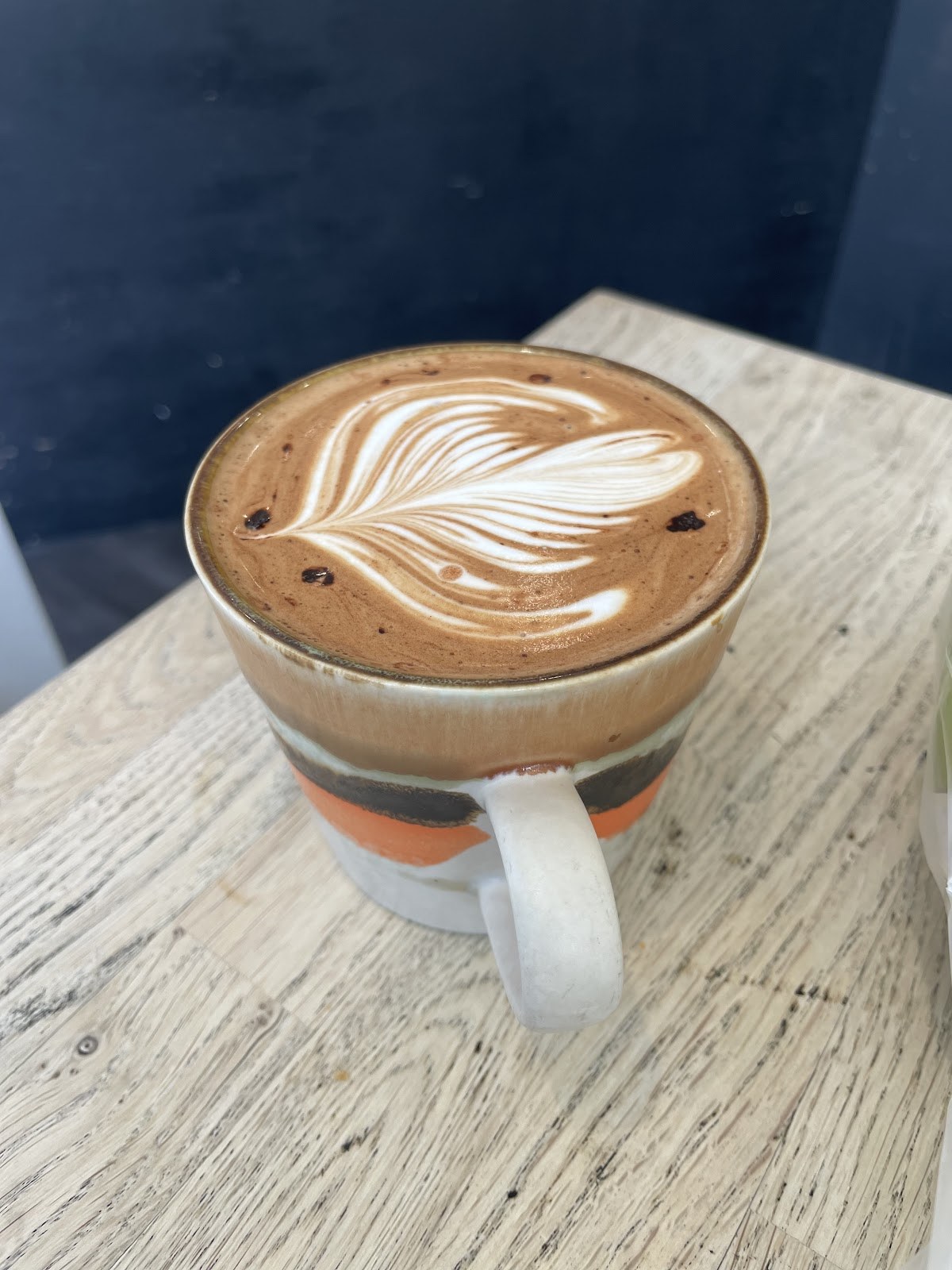 A coffee with feathered latte art on a wooden table at Canopy